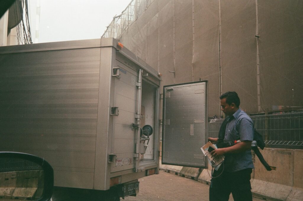 pexels-photo-8696371-8696371 A logistics worker in a blue shirt checking a cargo truck on a city street. Industrial background suggests transportation and delivery.